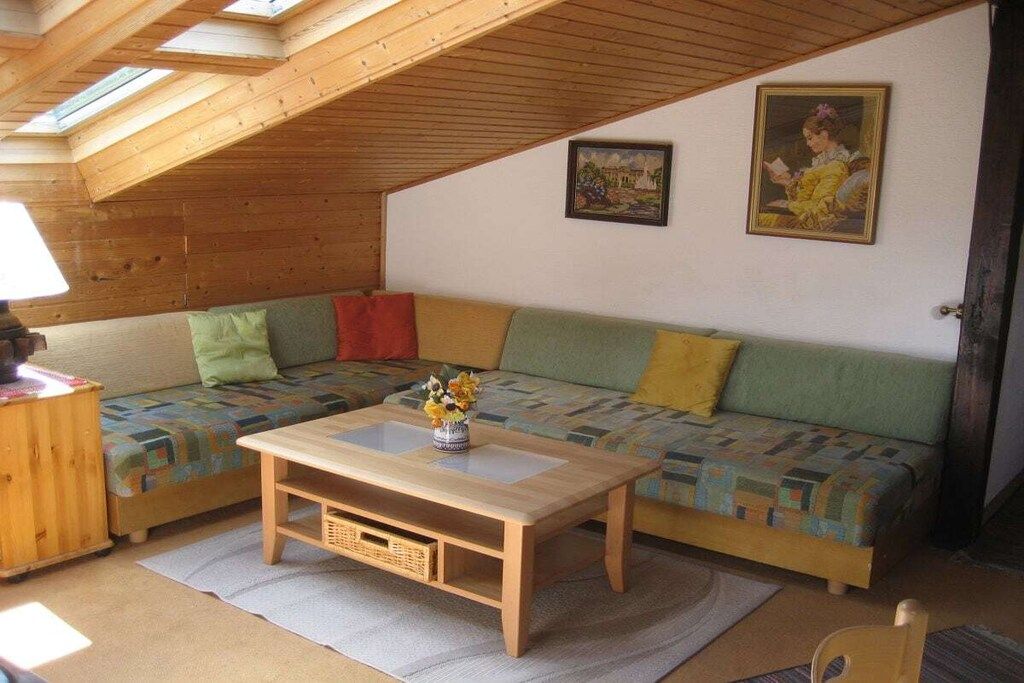 Ein gemütliches Zimmer mit Holzboden, einem Sofa mit bunten Kissen, einem kleinen Holztisch und einem Bild an der Wand.