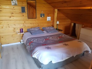 A wooden-paneled room with a bed, a bedside table, a lamp, and a mirror. - Chalet "Le Cocon": Mountain View, Private Terrace & Wi-Fi (Foncine le Haut)