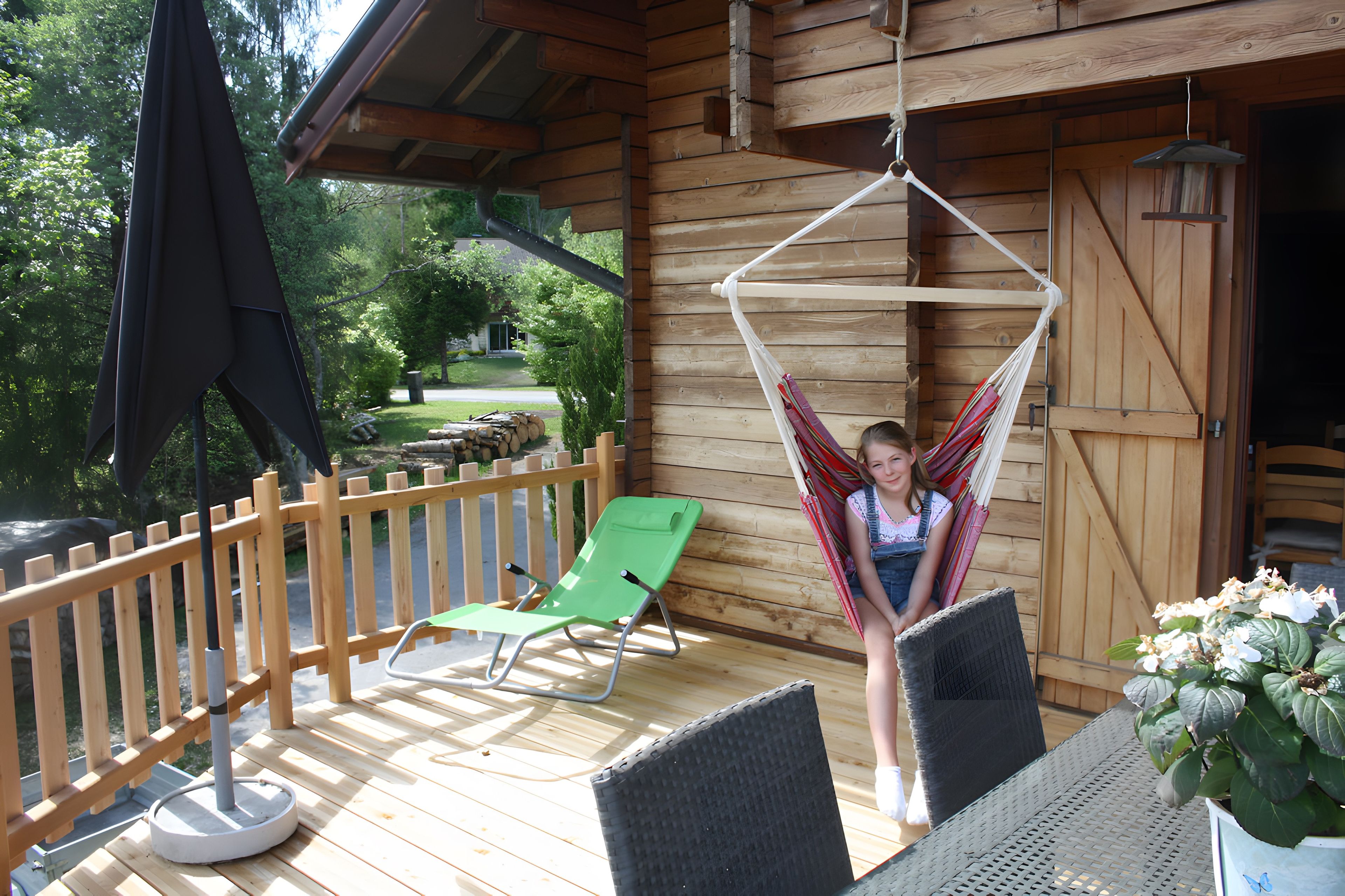 A wooden deck with a hammock, a green lounge chair, and a table with chairs.