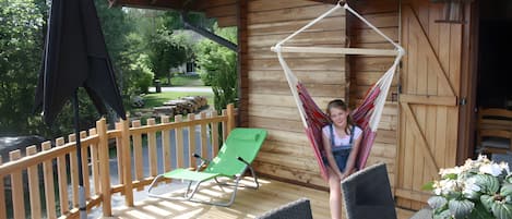 A wooden deck with a hammock, a green lounge chair, and a table with chairs.
