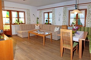 A living room with a sofa, a coffee table, a dining table with chairs, and a radiator. - Fellhorn in the House of Narcissus (Riezlern)