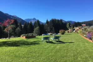 Eine grüne Freifläche mit zwei Stühlen und einem Tisch, umgeben von Bäumen und einem Berg im Hintergrund.