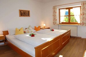 A double bed with a wooden frame, two bedside tables, a nightstand, a window with floral curtains, and a radiator. - Fellhorn in the House of Narcissus (Riezlern)