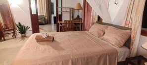 A neatly made bed with a folded towel, a wooden chair, a small potted plant, and a desk with a lamp. - Henz & Sia Tourist Residence – Your Island Home in Rodrigues 🌴 (Piments Reposoir Rodrigues)
