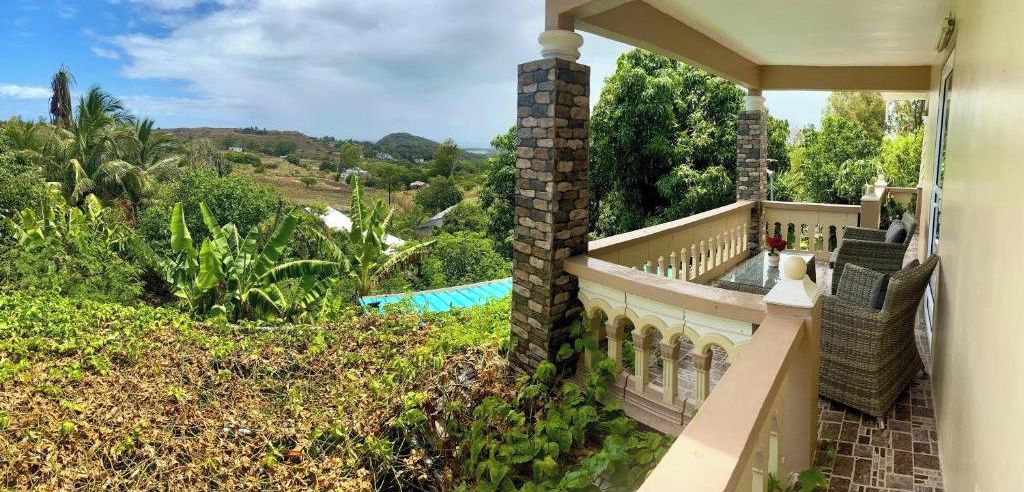 A balcony with a view of a lush landscape, a pool, and outdoor furniture.