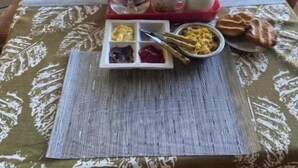 Una mesa dispuesta con artículos para el desayuno, incluyendo una jarrón, tazas, platos y una bandeja con comida.