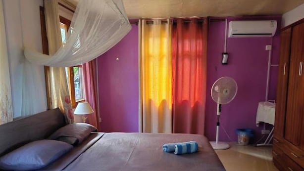 Una habitación con una cama, una mesita de noche con lámpara, un ventilador y un armario.