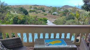 Un balcón con mobiliario de mimbre, una mesa con un mapa y vistas a un paisaje montañoso.