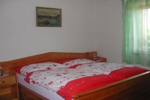 A bedroom with a wooden bed, a nightstand, a painting on the wall, and a window with a green curtain. - Holiday home with 3 bedrooms (St. Stefan ob Stainz)