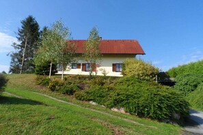 A two-story house with a red roof, surrounded by greenery and a clear sky. - Holiday home with 3 bedrooms (St. Stefan ob Stainz)