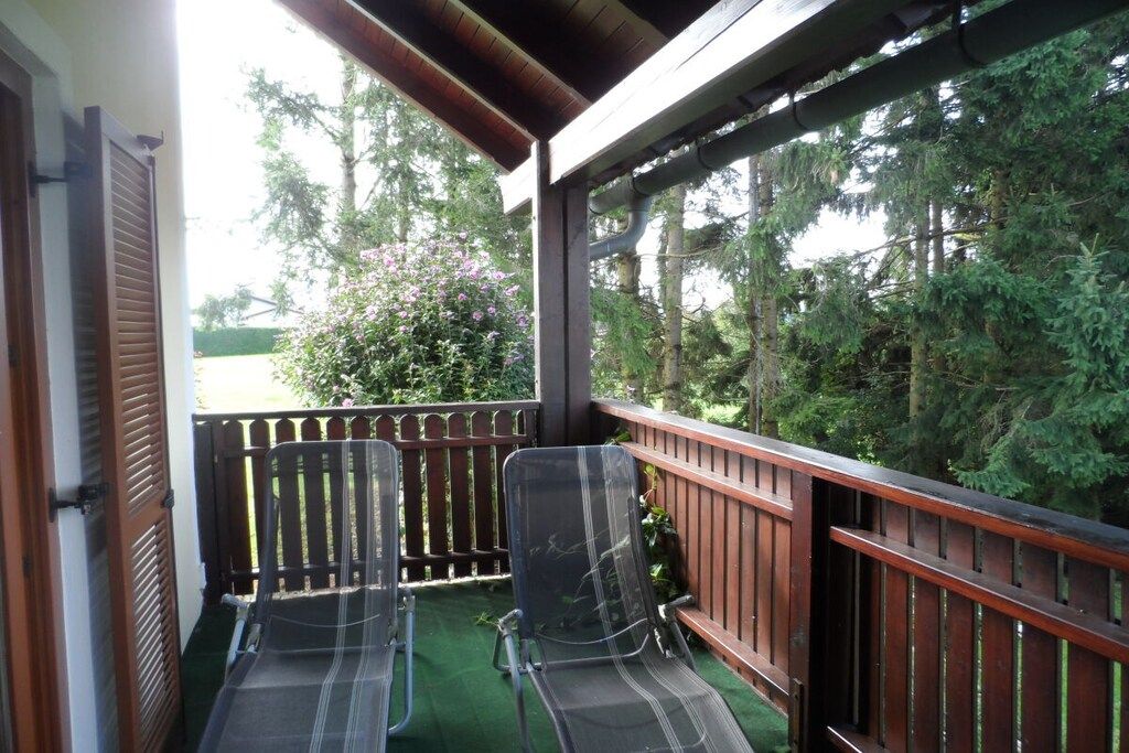 Varanda com duas cadeiras e guarda-corpo de madeira, com vista para um jardim com árvores e arbustos.