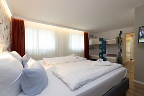 A hotel room with two beds, a bunk bed, a bathroom with a mirror, and a wall-mounted TV. - Little Suite Apartment 3 (Dresden)