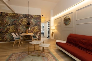 A modern living room with a red sofa, a dining table with chairs, a patterned wall, and a lamp. - Little Suite Apartment 3 (Dresden)