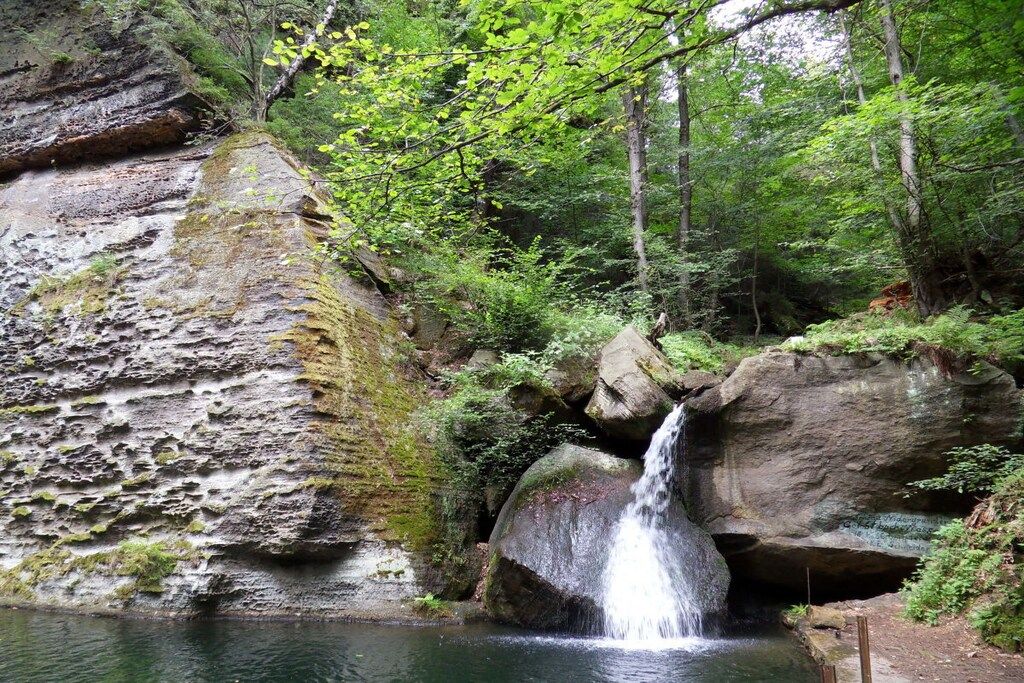 Ein natürlicher Wasserfall, umgeben von Felsen und viel Grün.