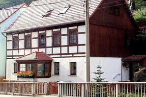 A traditional half-timbered house with a sloped roof, a small porch with a window, and a wooden fence in front. - Holiday apartment with 1 bedroom (Bad Schandau)