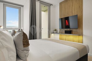 A modern hotel room with a large bed, a TV mounted on a wooden panel, and a view of the city through the window. - Skora by Kozystay - Cilandak (South Jakarta)