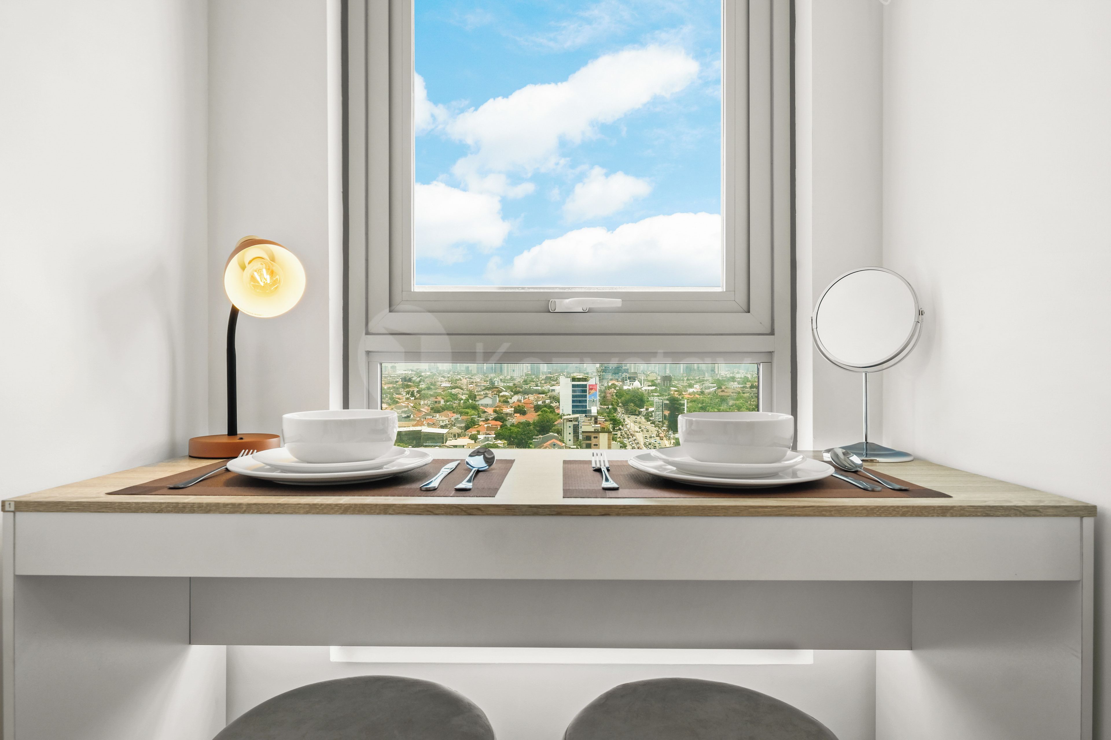 A modern room with a dining table set for two, a window with a city view, and a bedside table with a lamp and a mirror.