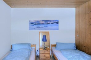Quarto com duas camas, teto de madeira, um quadro na parede e luminária de cabeceira.