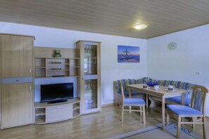 Ein Zimmer mit Fernseher, Holzschränken, einem Esstisch mit Stühlen und einem Bild an der Wand.