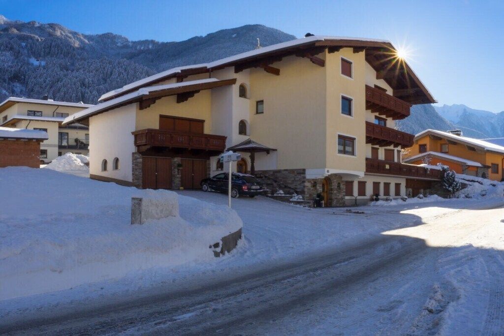 Un bâtiment enneigé, doté d’un toit en pente, d’un balcon et ayant une chaîne de montagnes en arrière-plan.