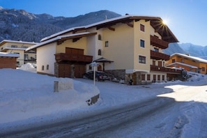 Ein schneebedecktes Gebäude mit geneigtem Dach, einem Balkon und einem Berg im Hintergrund.