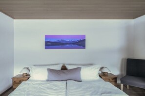Ein Schlafzimmer mit einem Bett, zwei Nachttischen, einem Sessel und einem Wandbild.