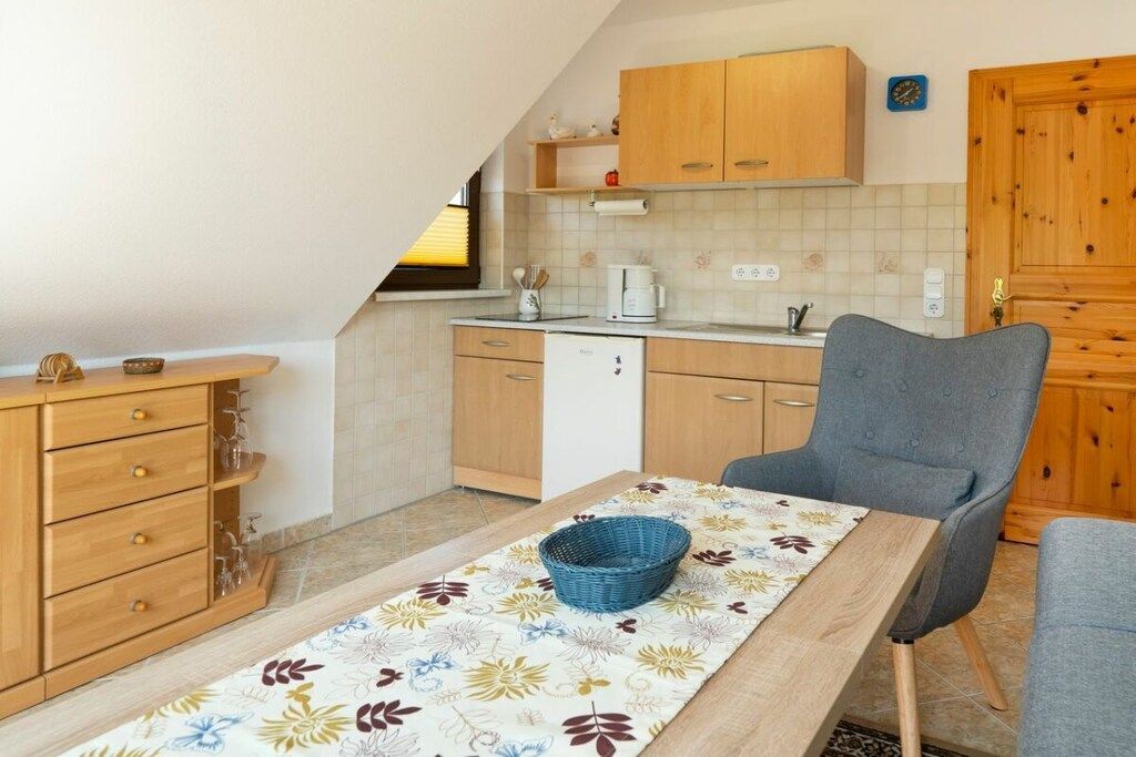 Eine kleine Küche mit Holzausbau, einem Esszimmertisch und einem blauen Korb sowie einem grauen Stuhl.