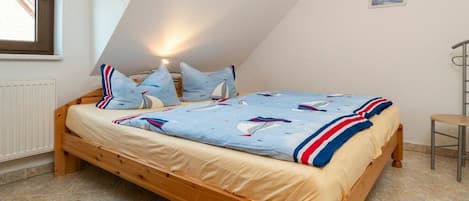 Un dormitorio con techo inclinado, una cama de madera, un ventanal con cortinas y un radiador.