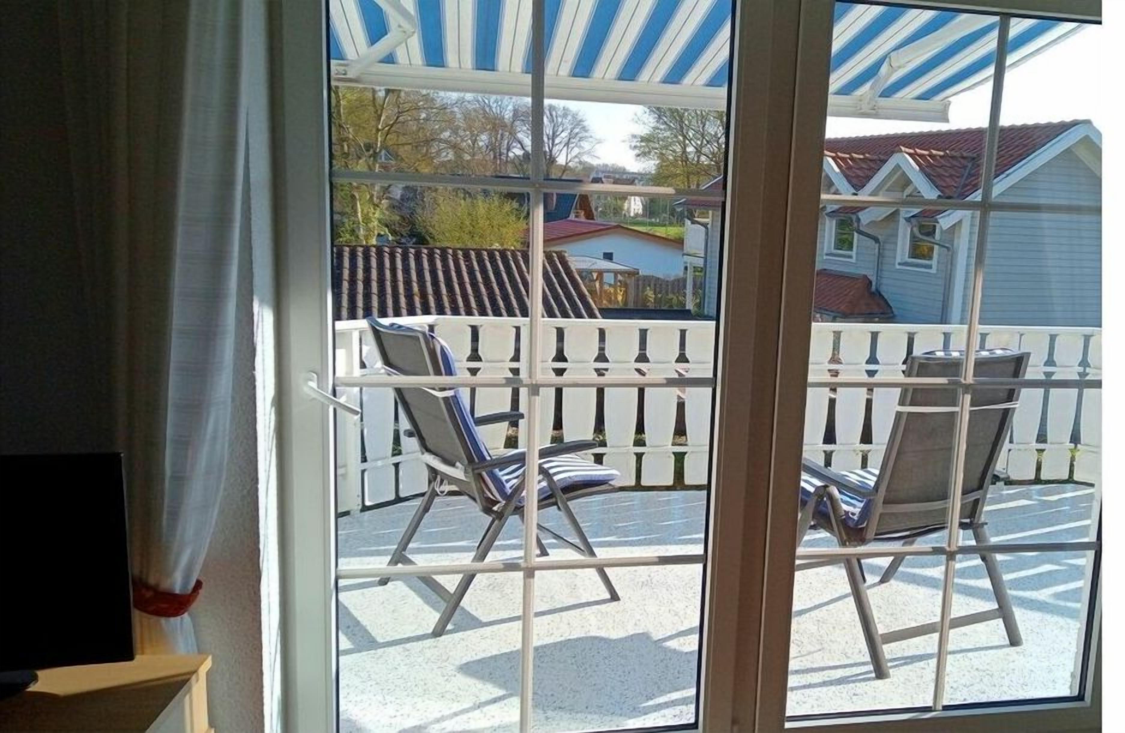 A room with a large window overlooking a balcony with two chairs and a table.