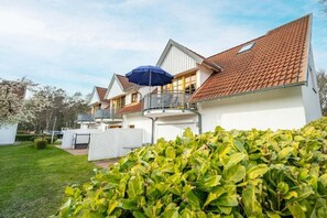 Een woongebouw met een pannendak, een overdekt terras met een blauwe parasol, en een verzorgd gazon.