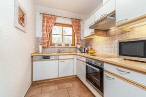 Eine kompakte Küche mit weißen Schränken, einem Einbauofen, einer Mikrowelle und einem Fenster mit Vorhängen.