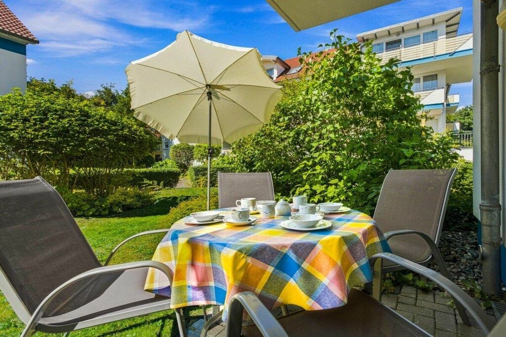 Un espace de restauration en plein air avec une table dressée pour quatre personnes, entourée de chaises, et protégée par un grand parasol.