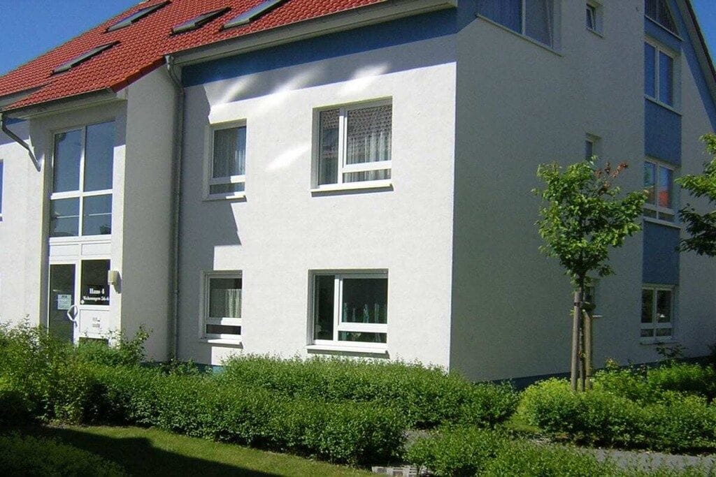 A multi-story building with a red-tiled roof, white exterior walls, and multiple windows.