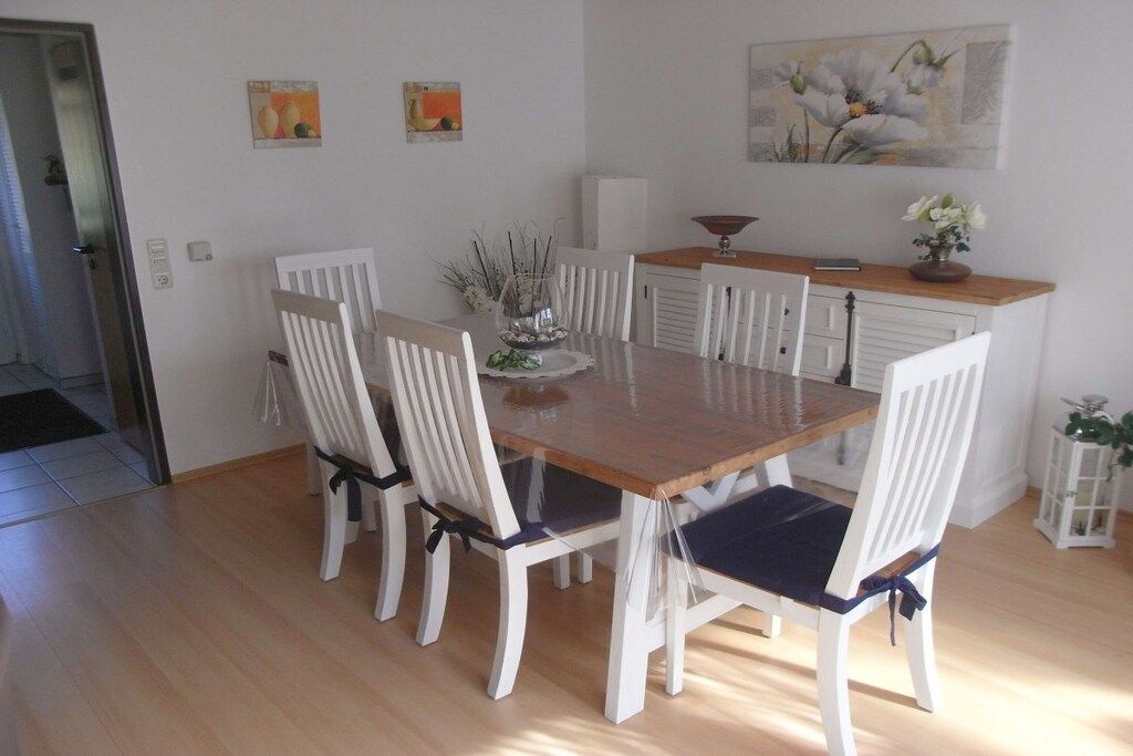Un coin repas avec une table en bois et des chaises blanches, un petit meuble et un tableau accroché au mur.