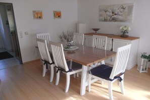 A dining area with a wooden table and white chairs, a small cabinet, and a painting on the wall. - Holiday home with 1 bedroom (Krummhörn - Greetsiel)
