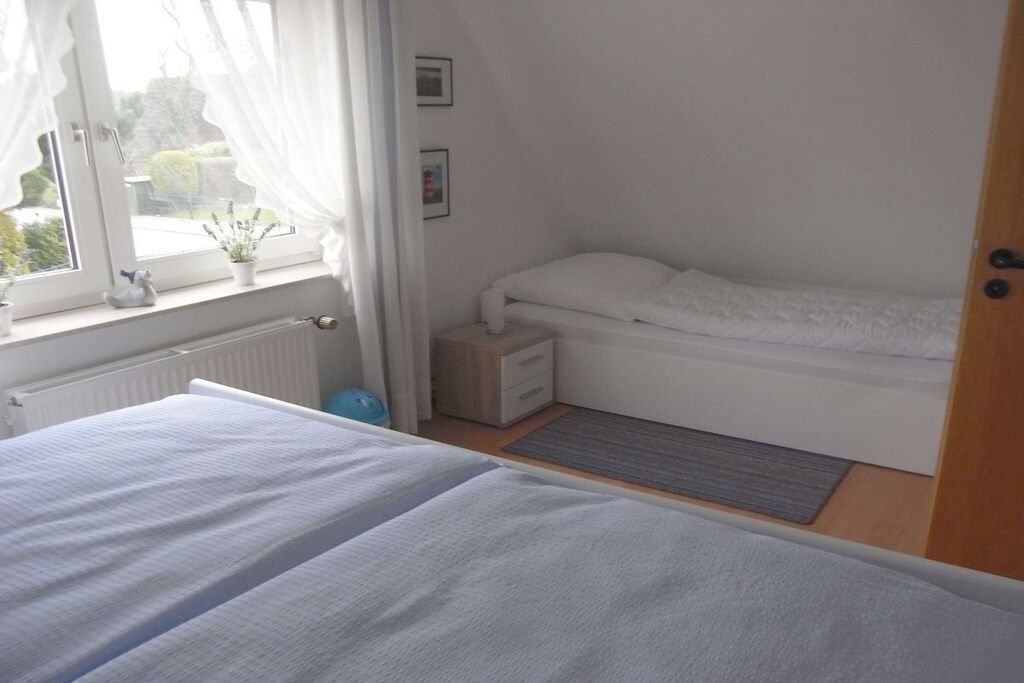 Une chambre à coucher avec un lit, une table de chevet, une fenêtre avec des rideaux et un radiateur.