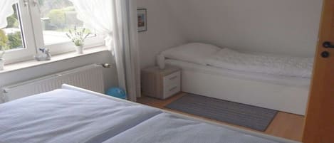 Une chambre à coucher avec un lit, une table de chevet, une fenêtre avec des rideaux et un radiateur.