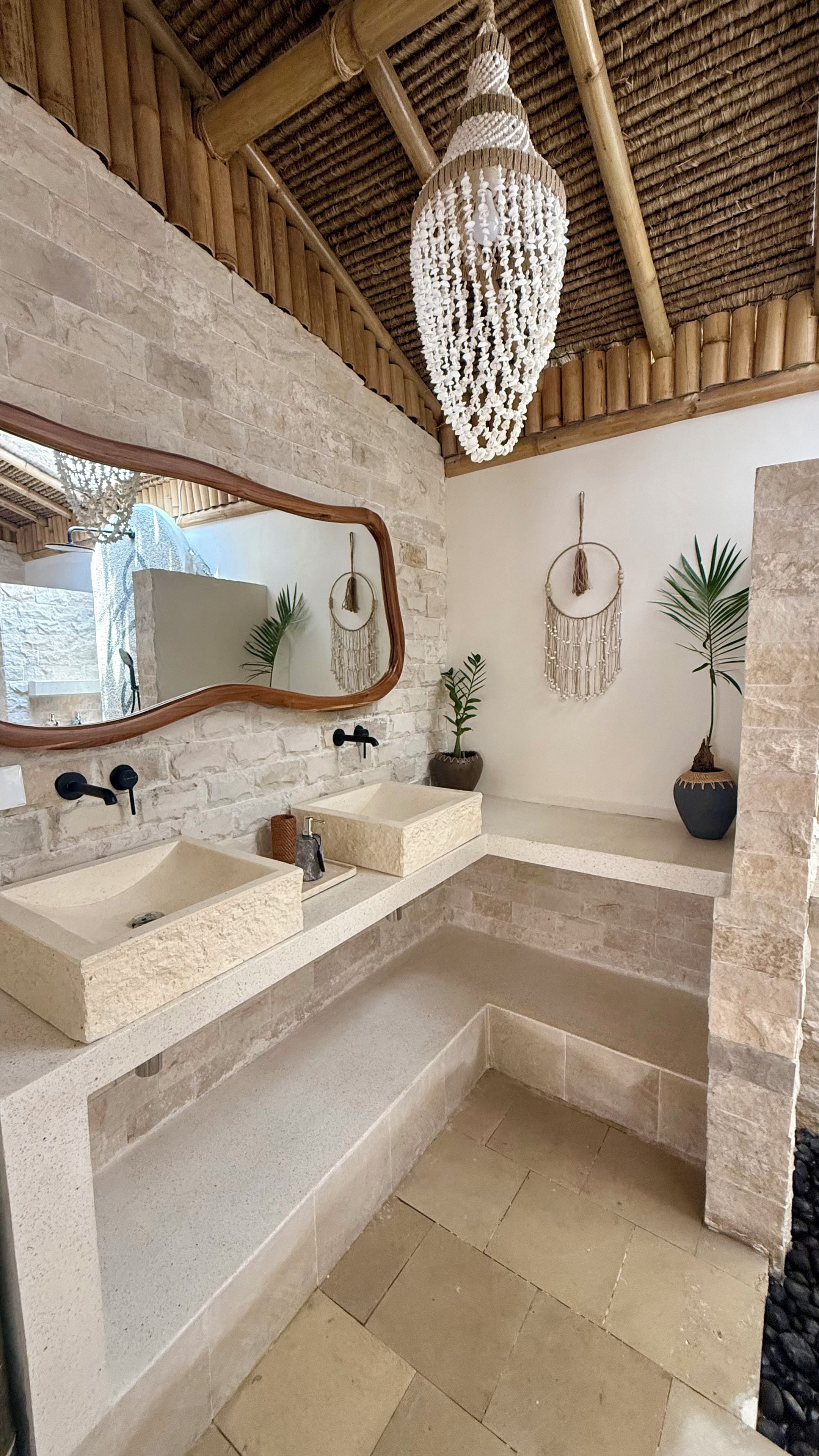 A bathroom with a stone sink, a mirror, a hanging light fixture, and a wall-mounted dreamcatcher.