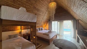 A room with a high ceiling, wooden beams, a bed with a canopy, a bedside table with a lamp, and a view of a swimming pool through a window.