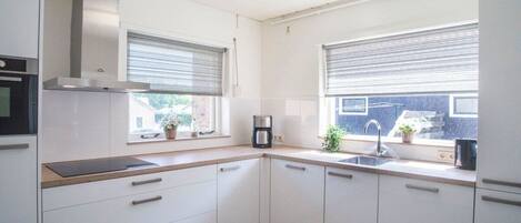Una cocina moderna con armarios blancos, una campana extractora de acero inoxidable, una cafetera y un ventanal con persianas.
