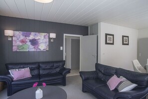 A room with two black leather sofas, a round coffee table with pink flowers, and a wall with a floral painting and two framed pictures. - Holiday home with 3 bedrooms (Zoutelande)