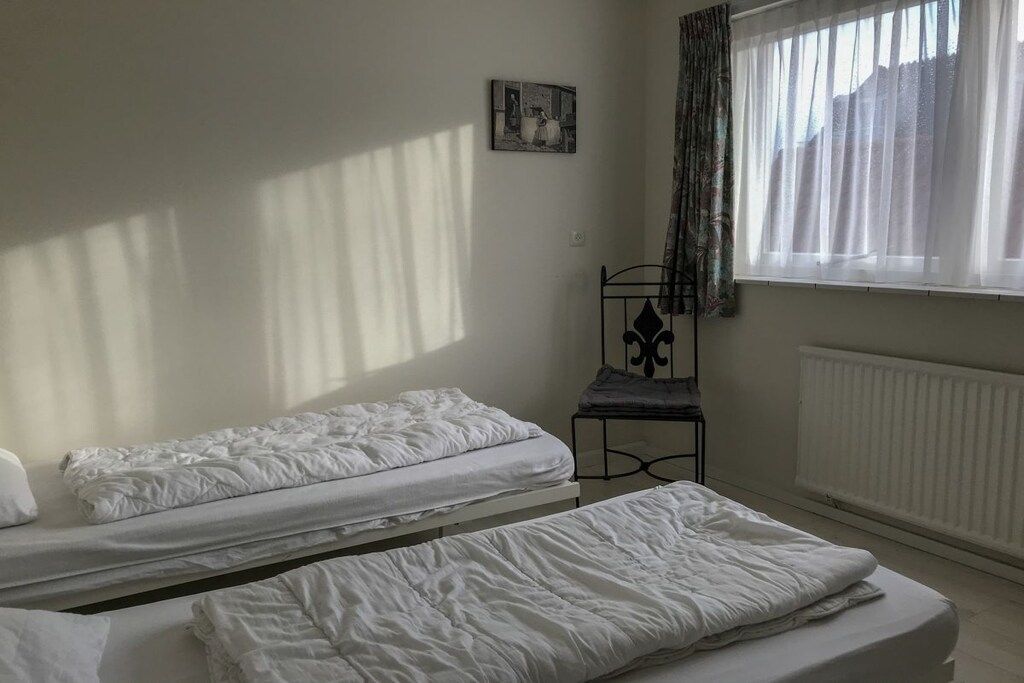 Una habitación con dos camas individuales, un radiador, una silla y una ventana con cortinas.