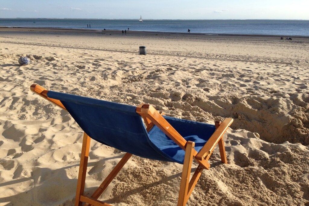 Una platja amb una cadira blava i un petit cubell de brossa.