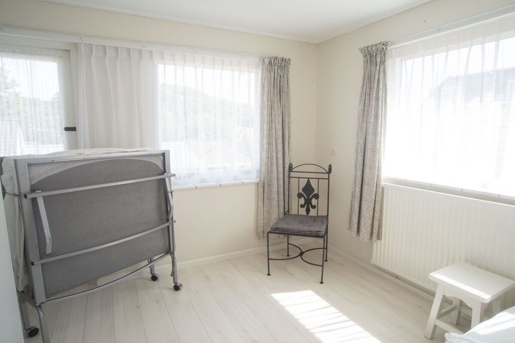 A room with a metal bed frame, a small white stool, and a chair with a cushion.