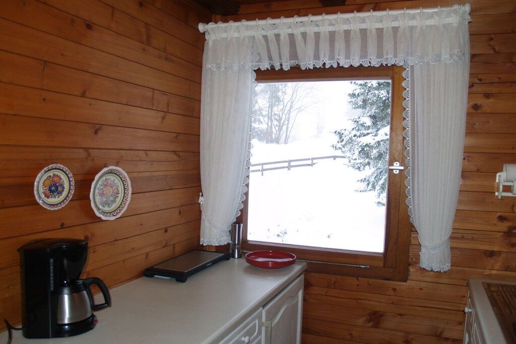 A wooden cabin interior with a window, a coffee maker, and two decorative plates on the wall.