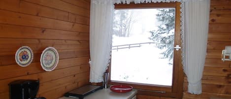 A wooden cabin interior with a window, a coffee maker, and two decorative plates on the wall.