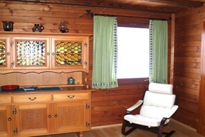 A wooden cabin interior with a wooden cabinet, a white chair, and a window with green curtains. - "Vogelsberg Holiday Magic" (Herchenhain)