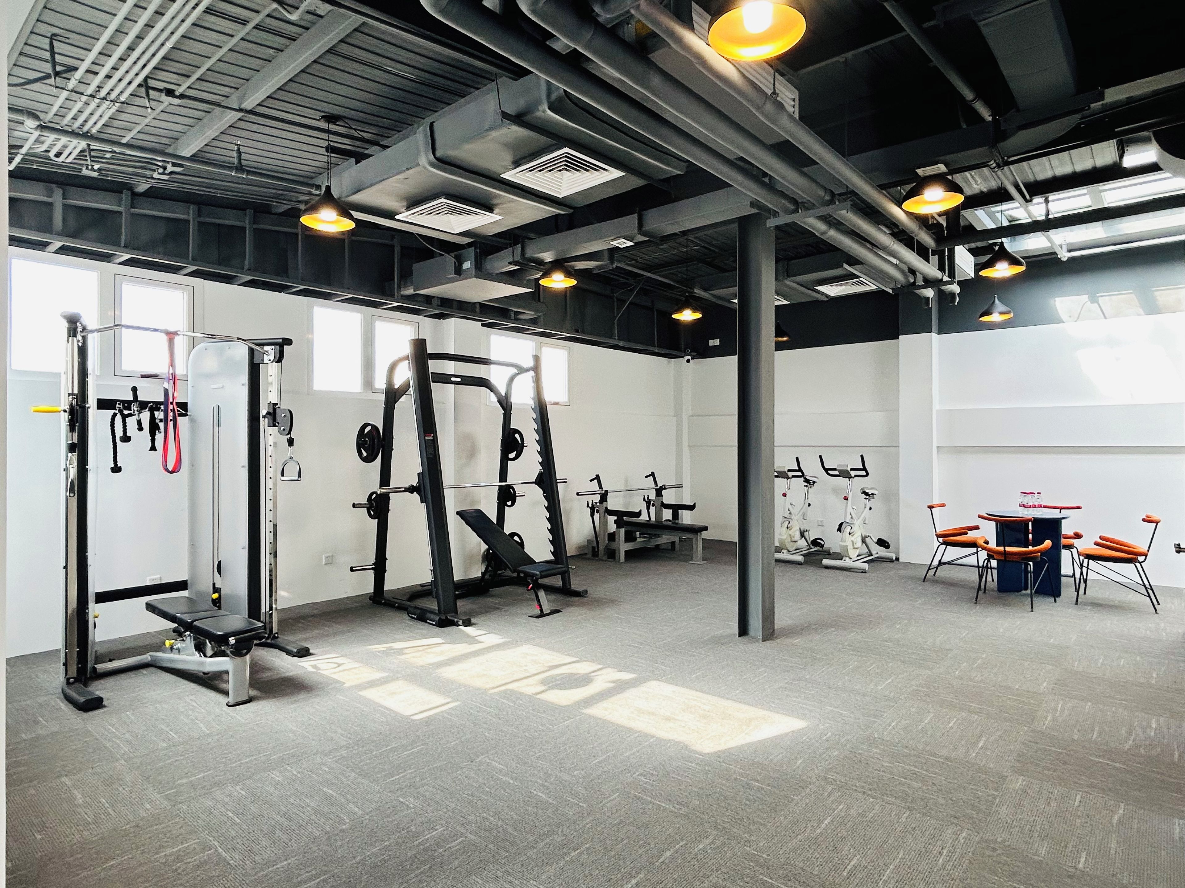 A gym with various exercise equipment, a bench, and a table with chairs.