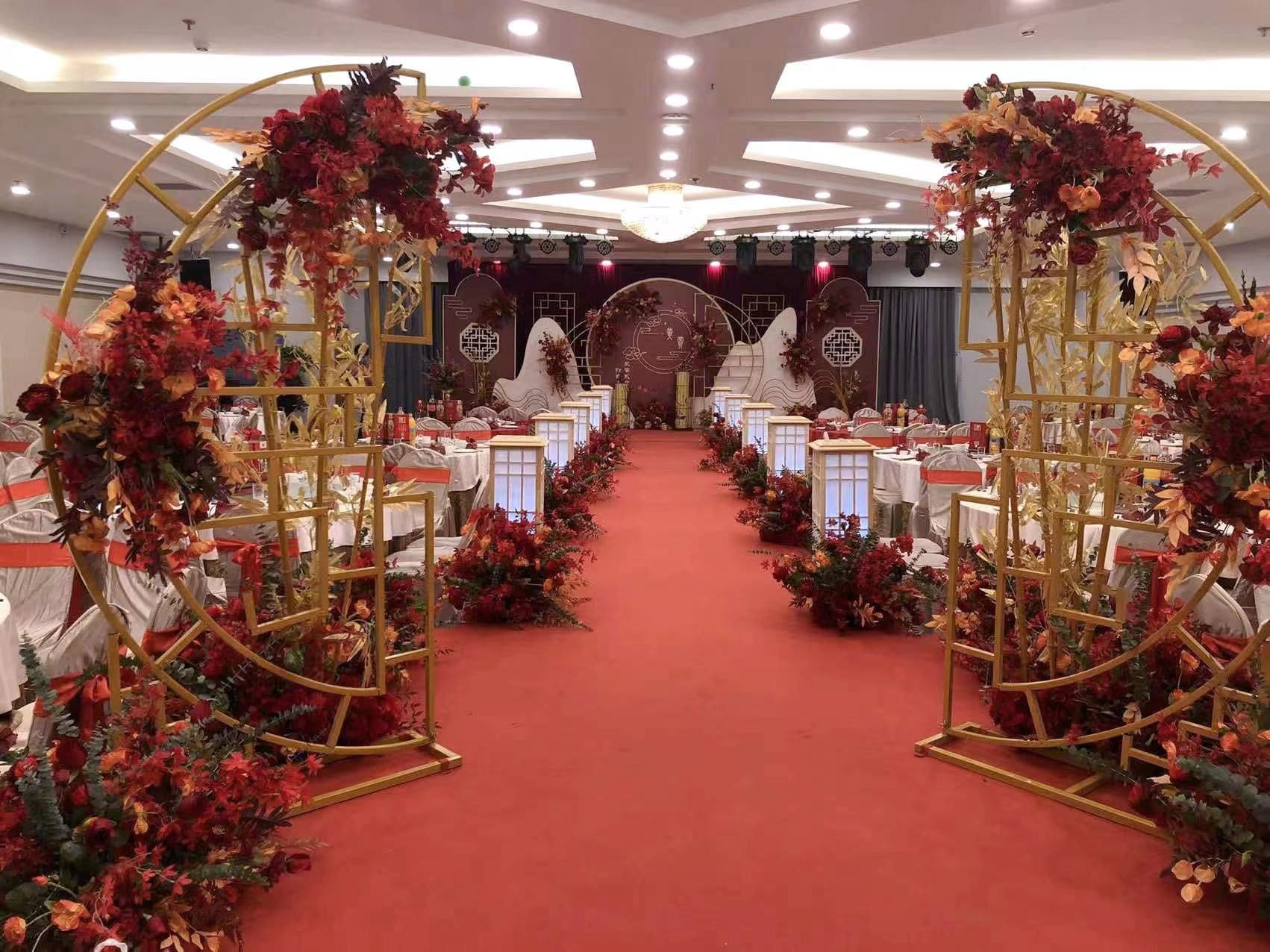A banquet hall with a red carpet, tables set for a formal event, and decorative floral arrangements.