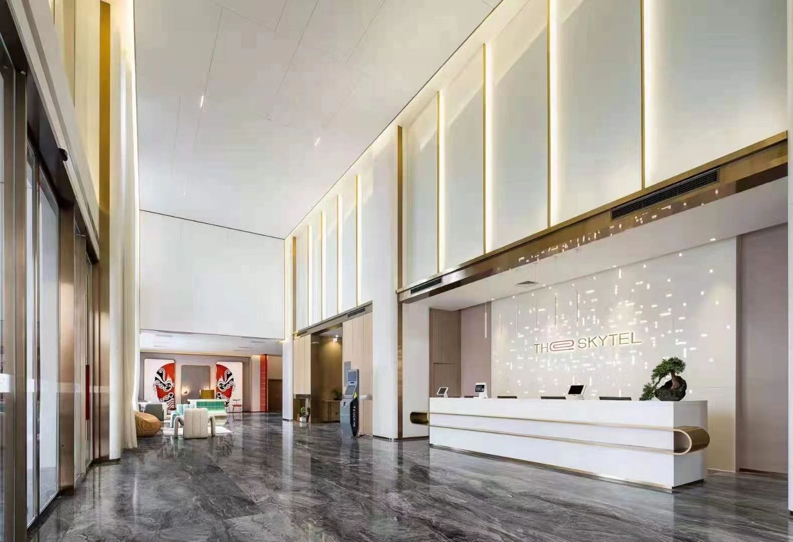 A modern hotel lobby with a reception desk, seating area, and a large window.